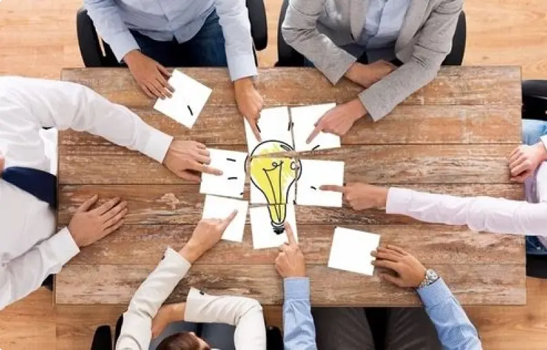 A group of business professionals collaborates around a table, with a light bulb symbolizing innovative ideas above them.